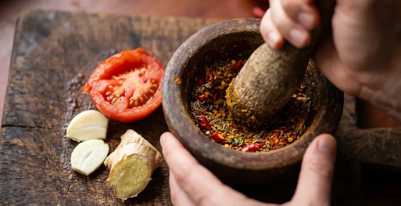 Gros plan sur des mains préparant un rougail avec pilon et mortier traditionnel