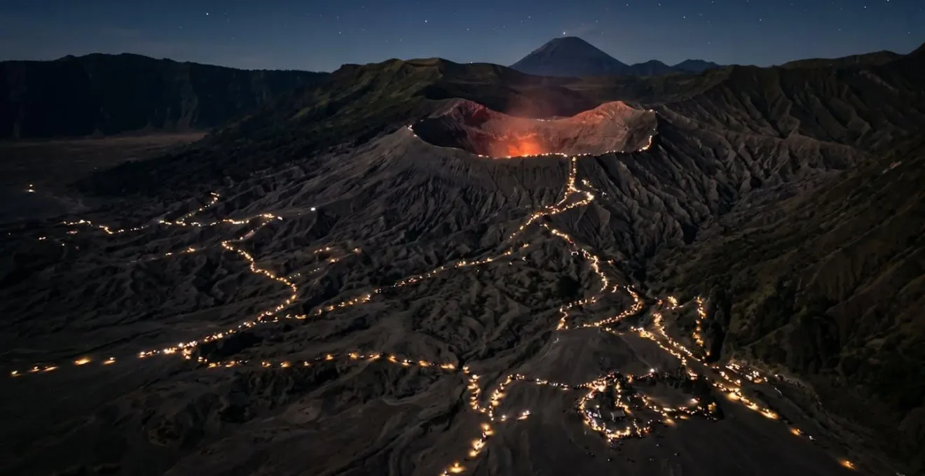 Vue aérienne nocturne montrant des centaines de points lumineux de lampes frontales sur les sentiers volcaniques