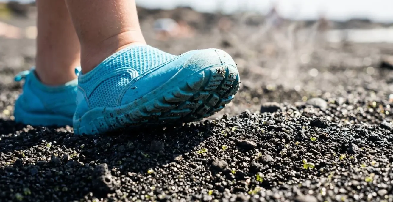 Gros plan sur des pieds d'enfants protégés par des chaussures d'eau colorées sur du sable noir volcanique brillant